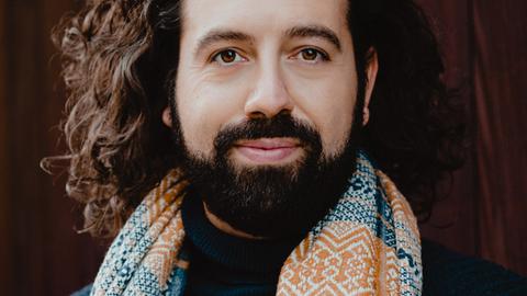 Stelios Chatziktoris trägt offenes, welliges Haar und einen Bart. Er schaut freundlich in die Kamera.