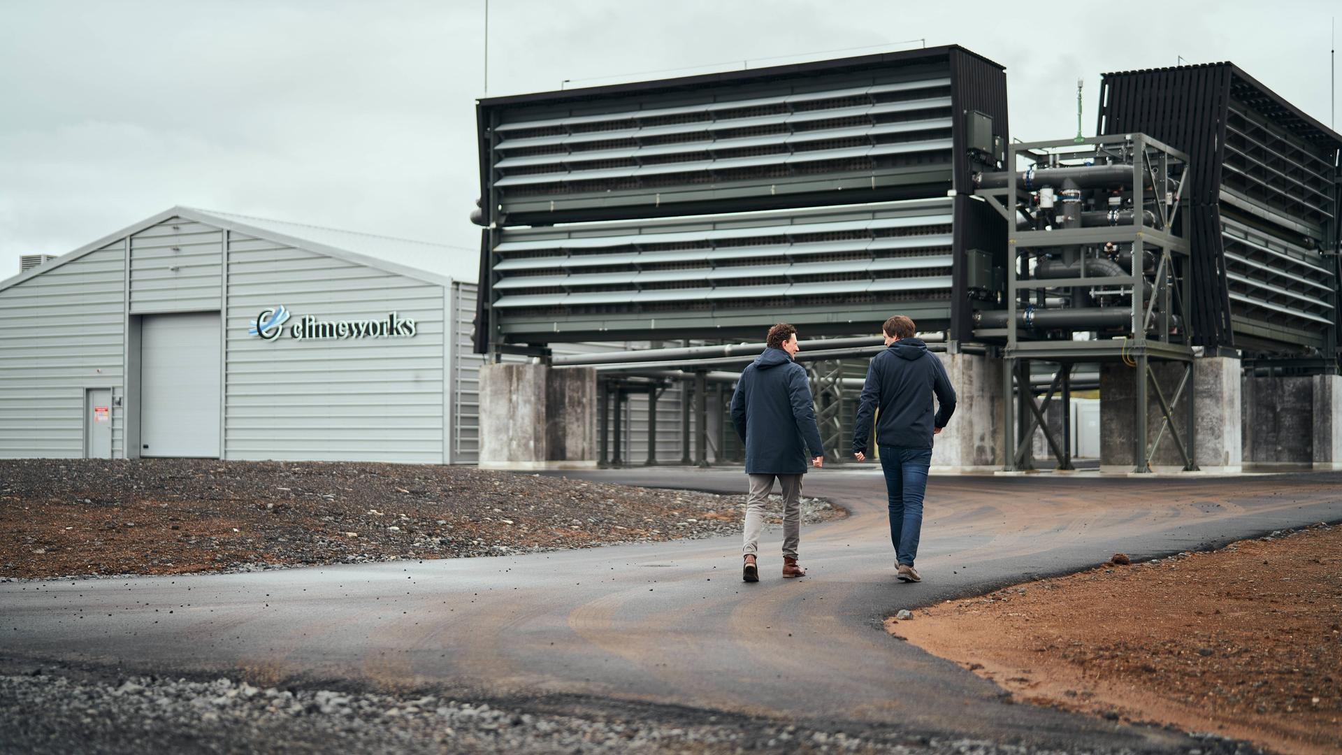 Zwei Männer gehen iin Richtung einer riesigen Filteranlage in Island, die das CO2 aus der Luft saugt

