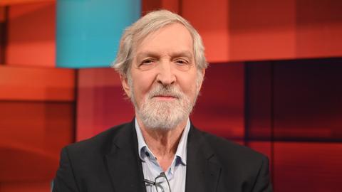 Shimon Stein sitzt in einem Fernsehstudio mit rot gekacheltem Hintergrund Shimon Stein sitzt in einem Fernsehstudio mit rot gekacheltem Hintergrund