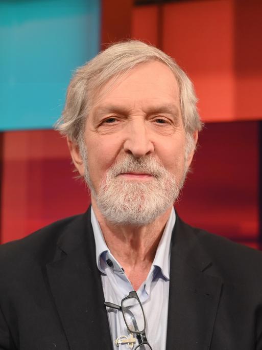 Shimon Stein sitzt in einem Fernsehstudio mit rot gekacheltem Hintergrund