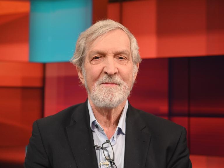 Shimon Stein sitzt in einem Fernsehstudio mit rot gekacheltem Hintergrund