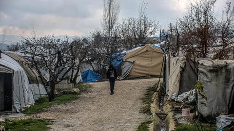 Eine Person mit hochgezogener Kapuze läuft eine unbefestigte Straße im Flüchtlingscamp entlang, die von Zelten gesäumt ist.