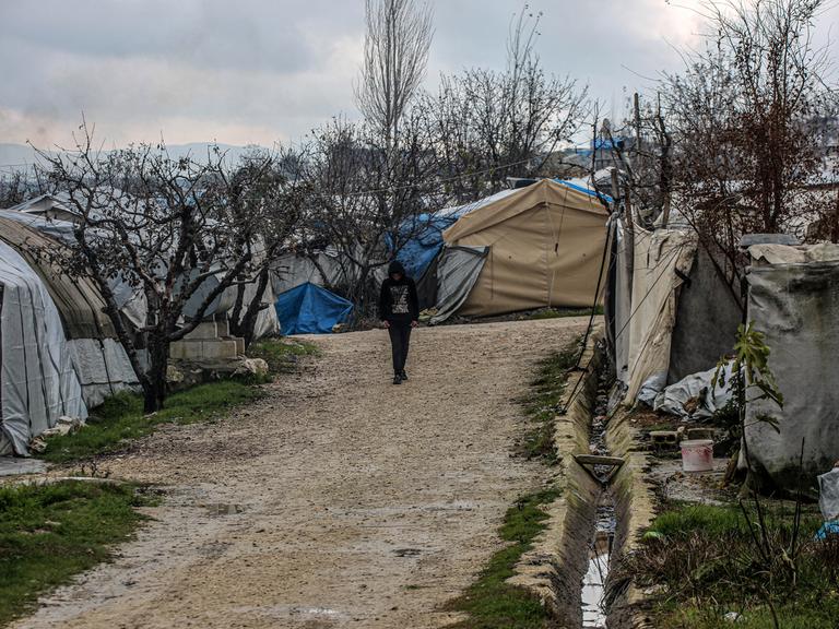 Eine Person mit hochgezogener Kapuze läuft eine unbefestigte Straße im Flüchtlingscamp entlang, die von Zelten gesäumt ist.