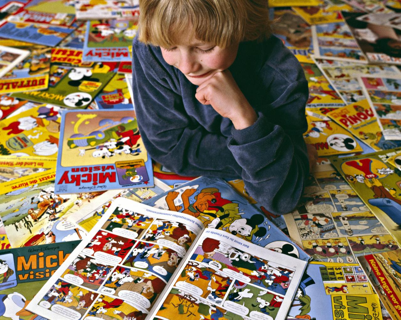 Ein Junge liegt auf zahlreichen Micky-Maus-Comicheften und liest ein Heft.