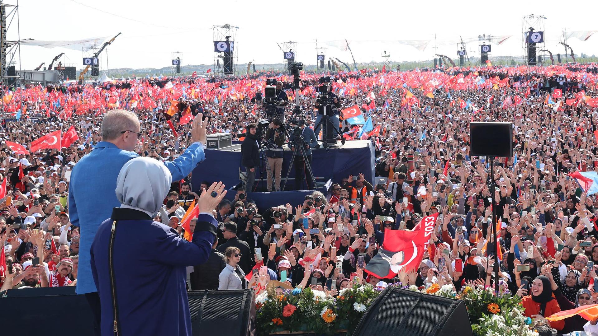 Erdogan und seine Frau stehen nebeneinander auf der Bühne und winken ins Publikum