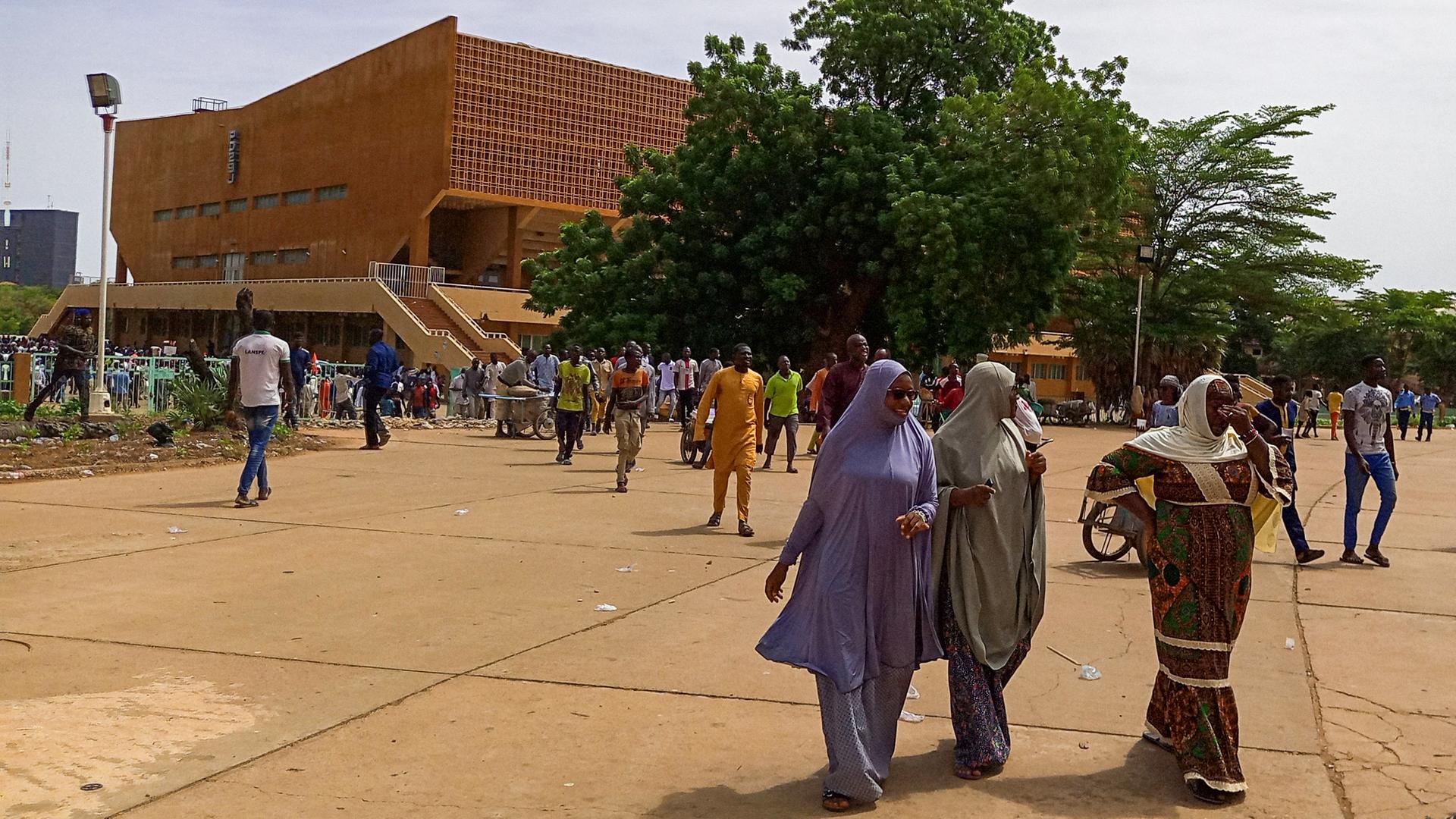 Einige Frauen aus Niger sind im Vordergrund zu sehen, im Hintergrund zahlreiche Passanten vor einem Fußballstadion