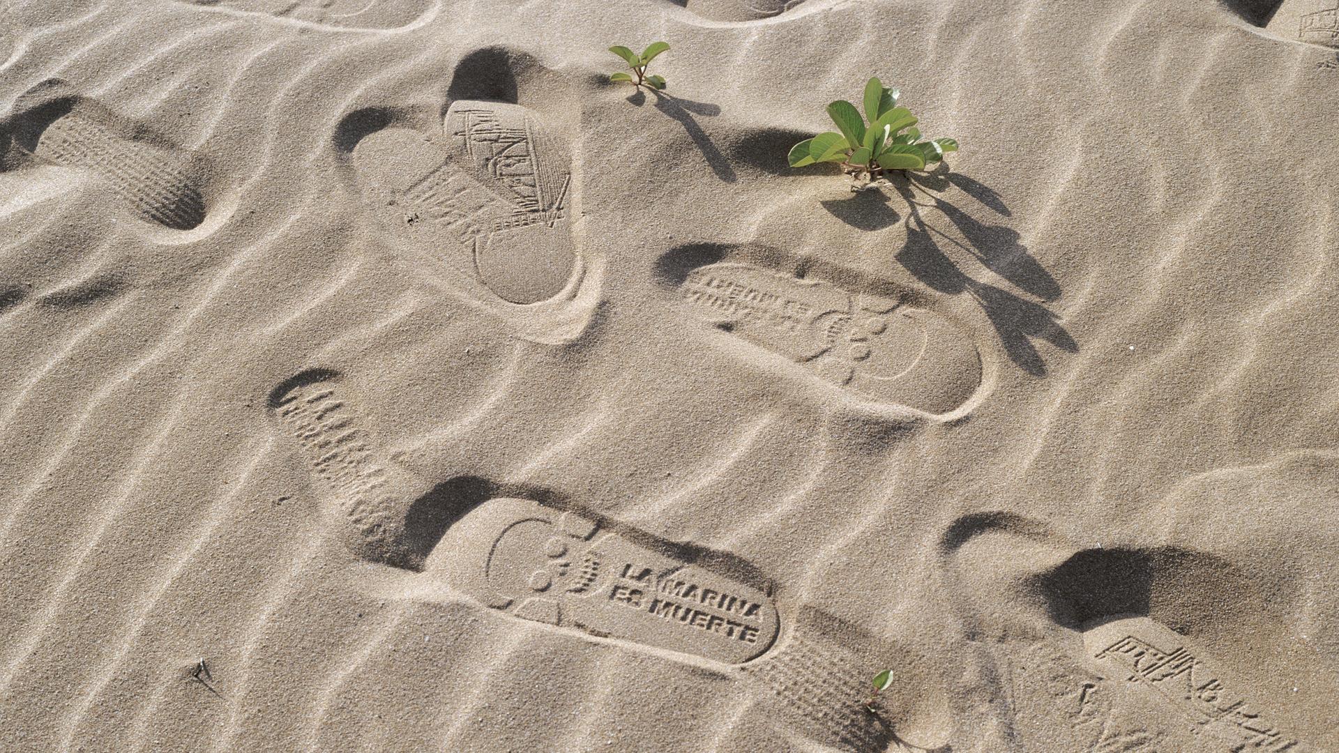 Fußspuren im Sand mit der Aufschrift "La Marina es Muerte" (Die Marine ist der Tod).