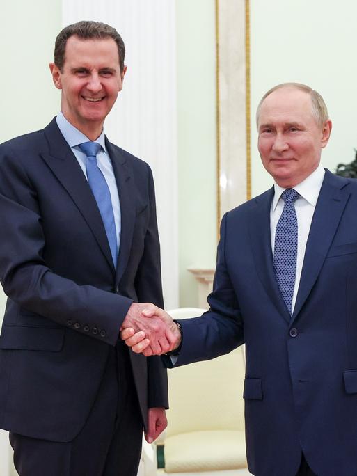 Wladimir Putin und Bashar al-Assad schütteln sich die Hände und lächeln in die Kamera.