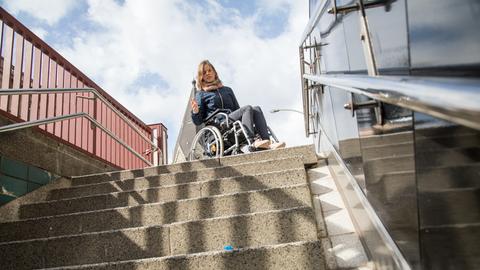 Eine Frau im Rollstuhl steht vor einer Treppe (gestellte Szene).