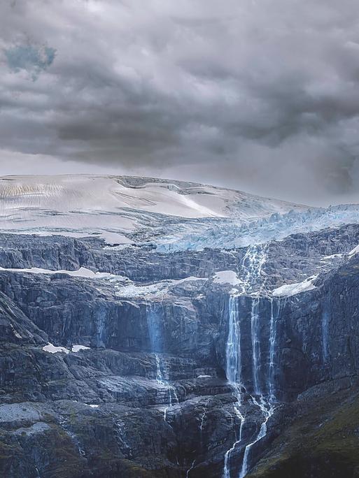 Das Wasser von einem schmelzenden Gletscher in Norwegen läuft an den Felswänden herab.