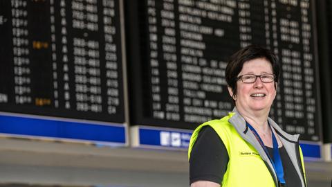 Die evangelische Pastorin Bettina Klünemann steht unter einer Anzeigetafel im Abflugbereich des Frankfurter Flughafens.