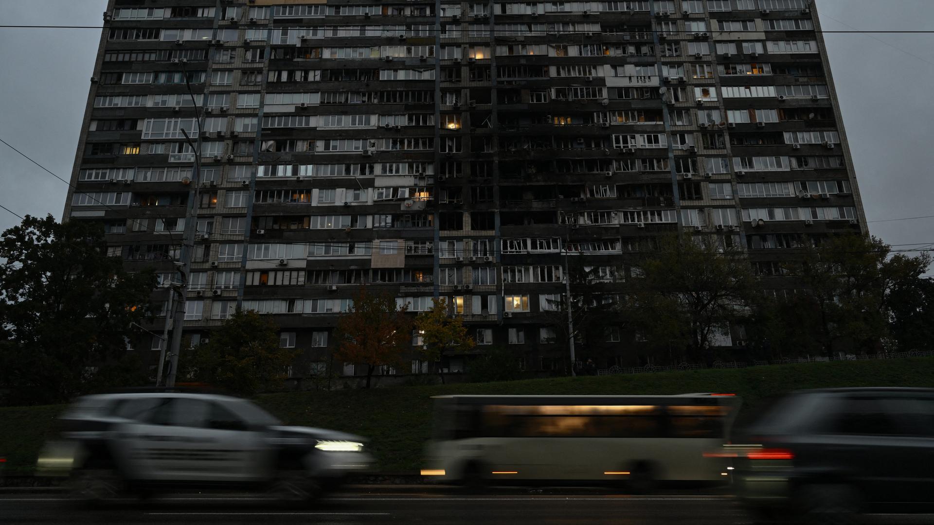 Autos fahren vor einem großen Wohngebäude, das von einem russischen Drohnenangriff beschädigt wurde.
