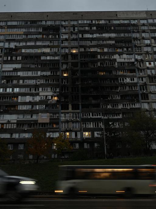 Autos fahren vor einem großen Wohngebäude, das von einem russischen Drohnenangriff beschädigt wurde.