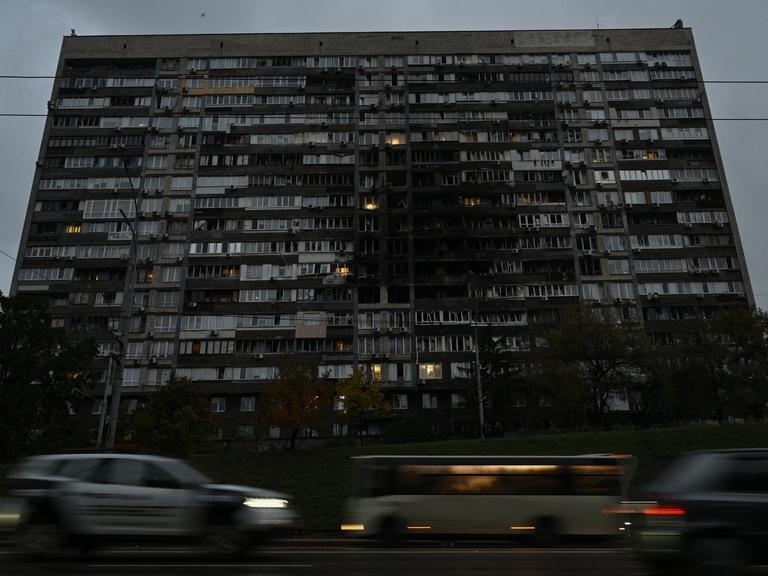 Autos fahren vor einem großen Wohngebäude, das von einem russischen Drohnenangriff beschädigt wurde.