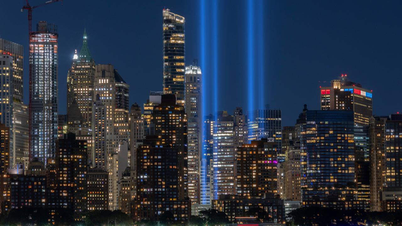 Zwei blaue Lichtsäulen ragen zwischen den Hochhäusern von New York bei Nacht in die Luft.