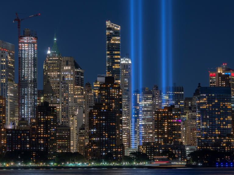 Zwei blaue Lichtsäulen ragen zwischen den Hochhäusern von New York bei Nacht in die Luft. Zwei blaue Lichtsäulen ragen zwischen den Hochhäusern von New York bei Nacht in die Luft.