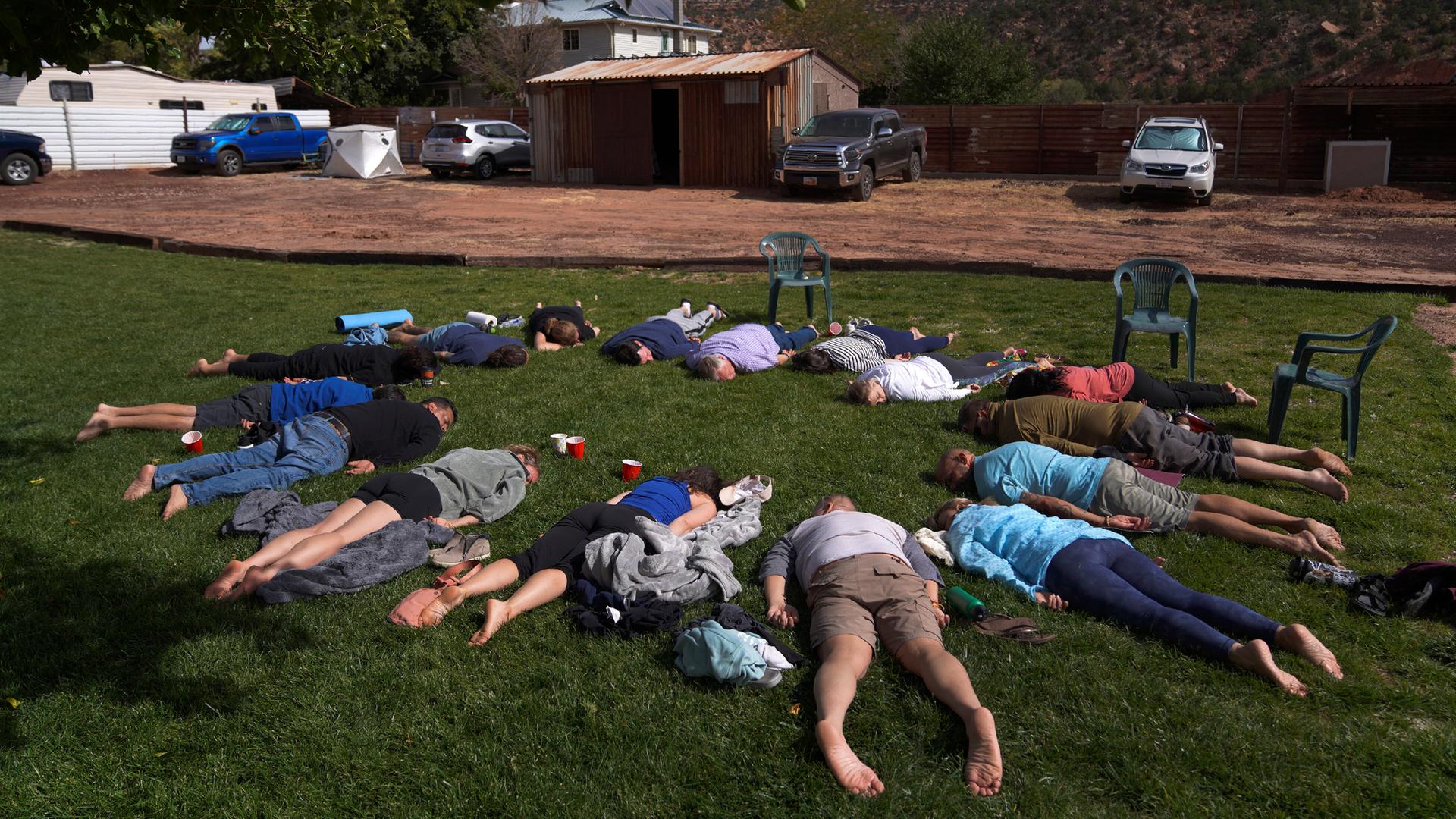 Teilnehmer liegen mit dem Gesicht nach unten im Gras während einer Zeremonie auf einem Ayahuasca Retreat in Hildale, Utah. Sie bilden einen Kreis, wobei ihre Köpfe zueinander zeigen. Teilnehmer liegen mit dem Gesicht nach unten im Gras während einer Zeremonie auf einem Ayahuasca Retreat in Hildale, Utah. Sie bilden einen Kreis, wobei ihre Köpfe zueinander zeigen.
