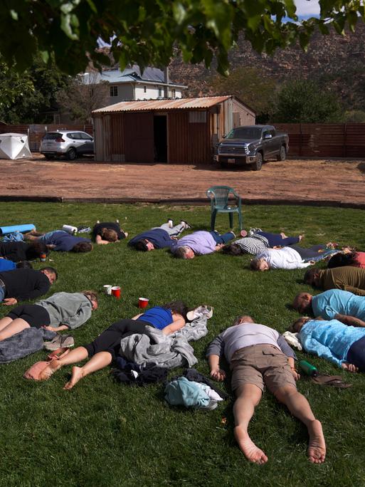 Teilnehmer liegen mit dem Gesicht nach unten im Gras während einer Zeremonie auf einem Ayahuasca Retreat in Hildale, Utah. Sie bilden einen Kreis, wobei ihre Köpfe zueinander zeigen.