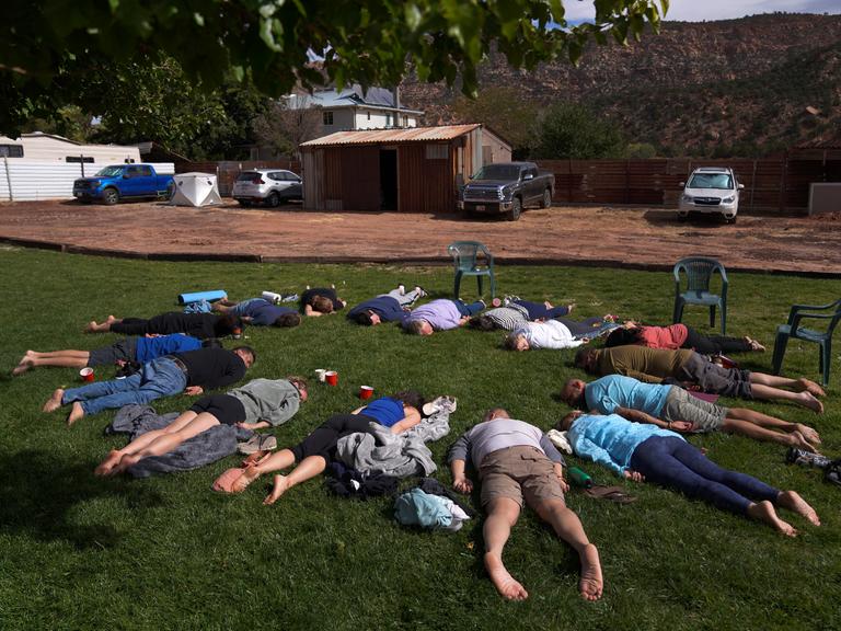 Teilnehmer liegen mit dem Gesicht nach unten im Gras während einer Zeremonie auf einem Ayahuasca Retreat in Hildale, Utah. Sie bilden einen Kreis, wobei ihre Köpfe zueinander zeigen.