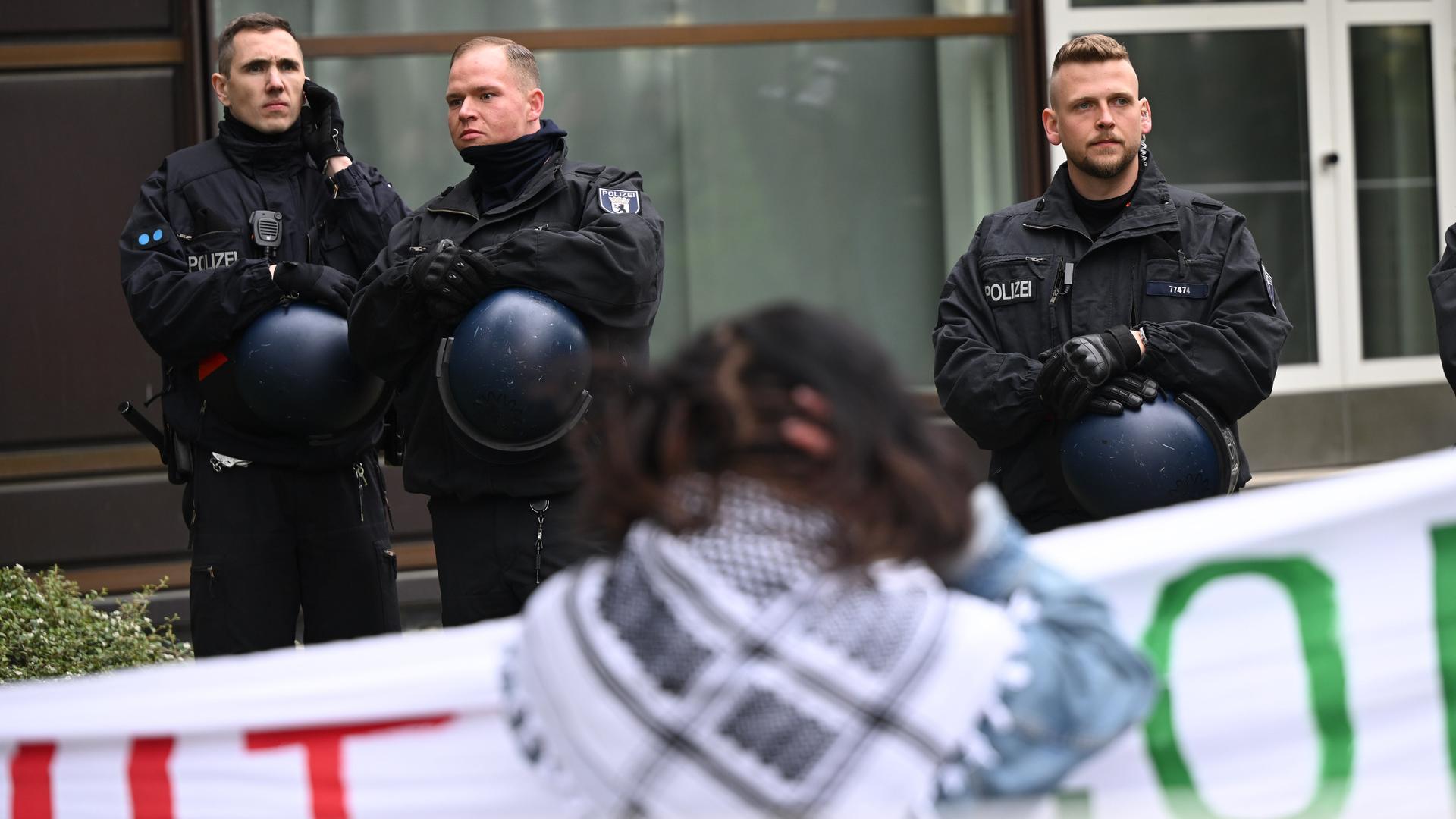 Teilnehmer stehen während einer pro-palästinensischen Demonstration auf dem Theaterhof der Freien Universität Berlin in der Nähe von Polizeibeamten. Im Hintergrund sind drei Polizisten, im Vordergrund eine Demonstrationsteilnehmende.