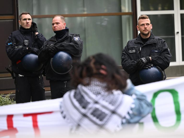 Teilnehmer stehen während einer pro-palästinensischen Demonstration auf dem Theaterhof der Freien Universität Berlin in der Nähe von Polizeibeamten. Im Hintergrund sind drei Polizisten, im Vordergrund eine Demonstrationsteilnehmende.