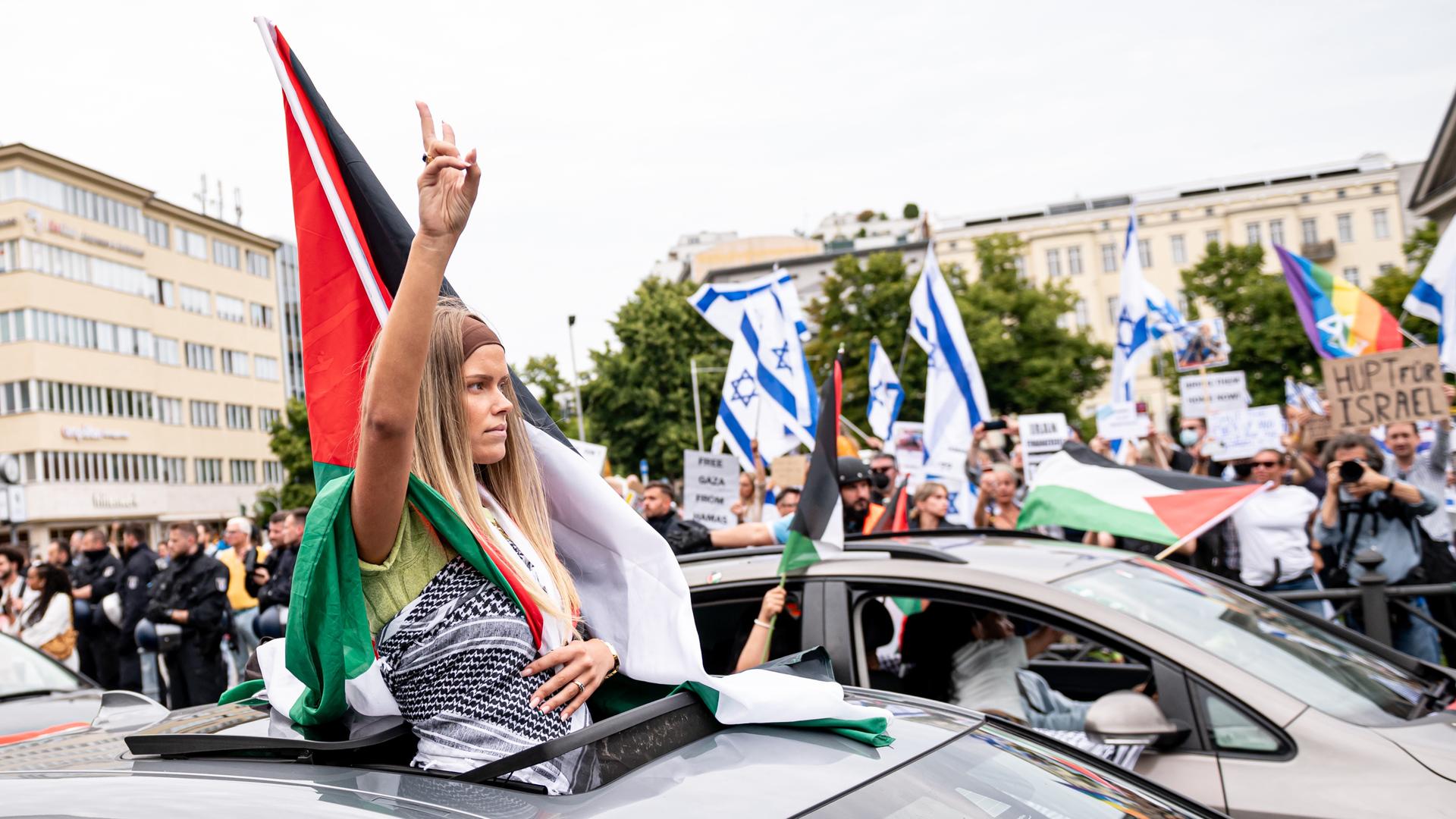 Eine Frau nimmt an einem propalästinensischen Auto-Korso teil und fährt an einer pro-Israel Demo vorbei.