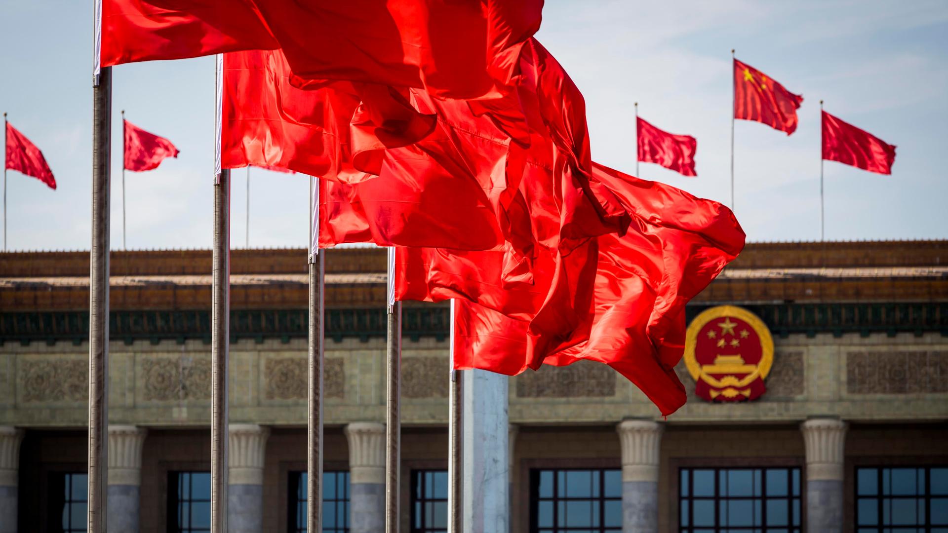 Mehrere chinesische Nationalflaggen wehen vor der Großen Halle des Volks in Peking. 
