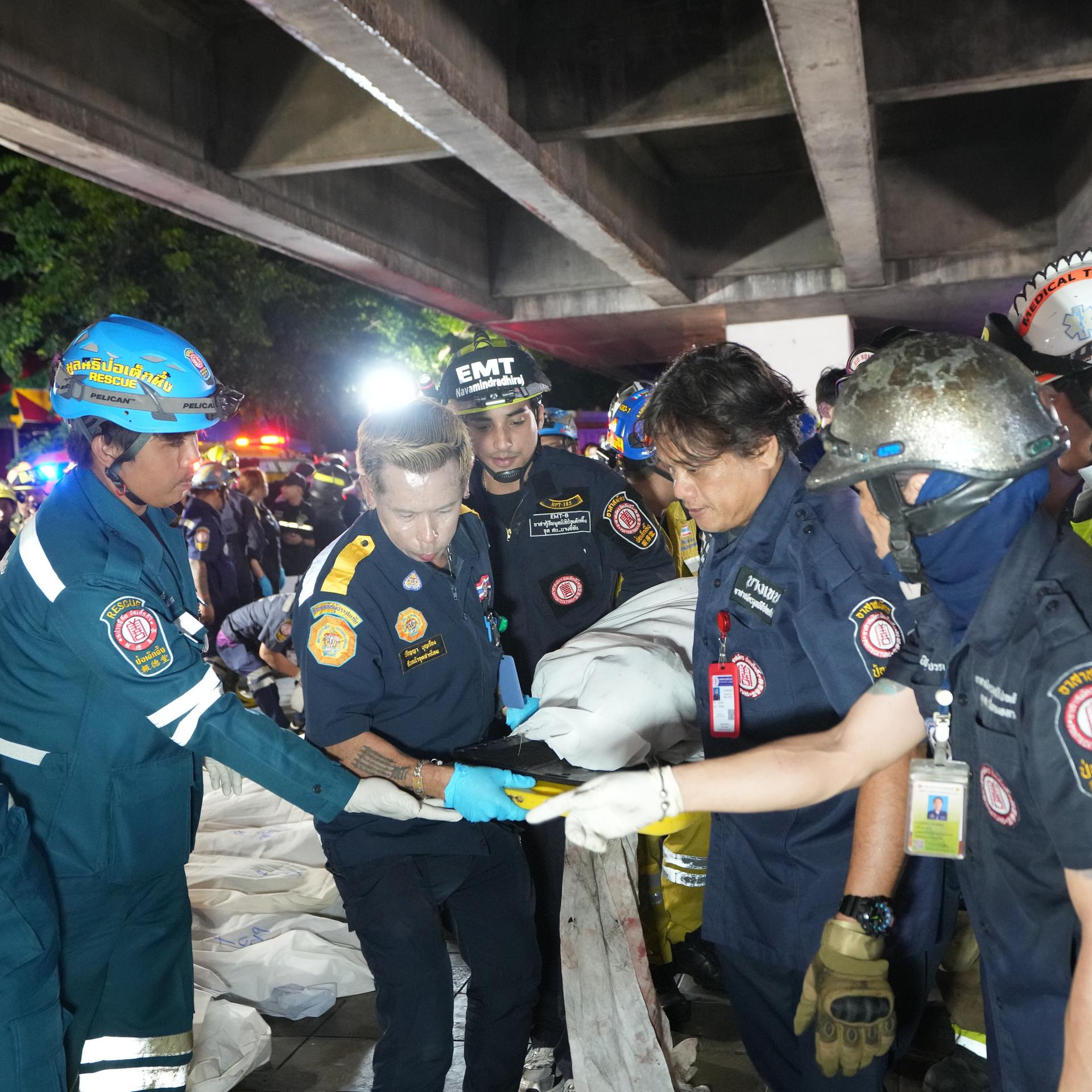 Rettungskräfte tragen eine Bahre mit einer Person darauf. Die Einsatzkräfte tragen Uniform und Schutzhelme.