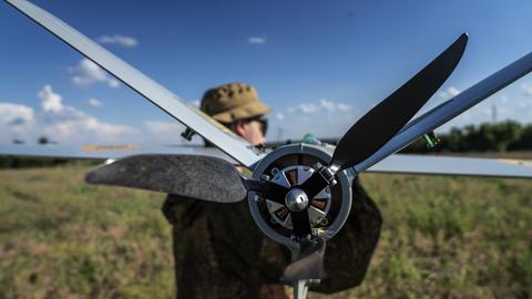 Ein Soldat steht auf einem Feld und hält eine Drohne in der Hand. Ein Soldat steht auf einem Feld und hält eine Drohne in der Hand.