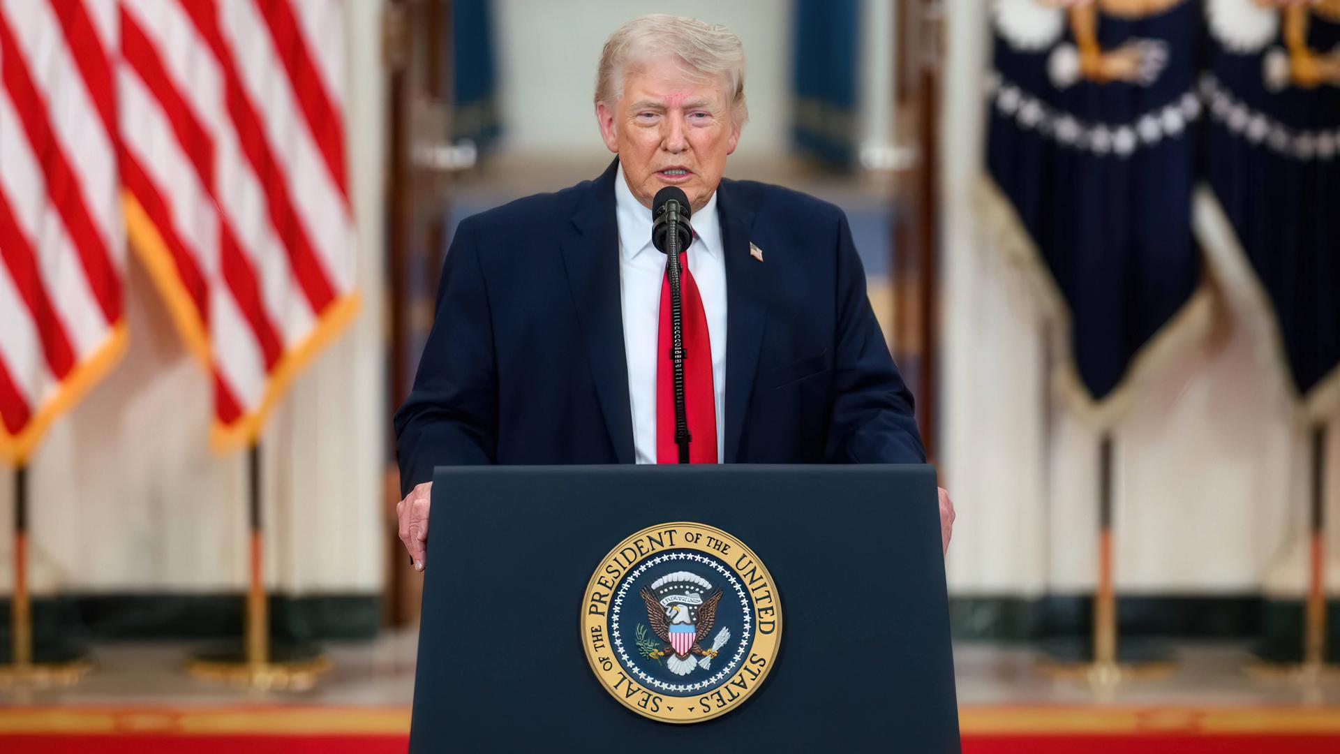 Donald Trump steht an einem Mikrofonpult. Neben ihm steht eine us-amerikanische Flagge Donald Trump steht an einem Mikrofonpult. Neben ihm steht eine us-amerikanische Flagge