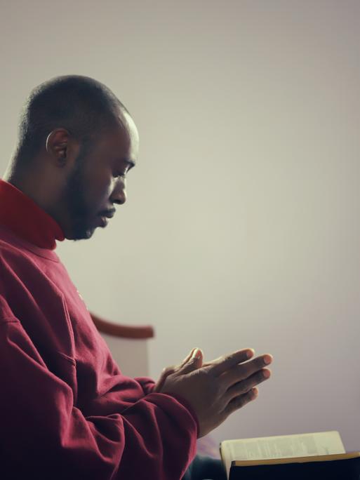 Eine afroamerikanische Person betet in einer Kirche in den USA.