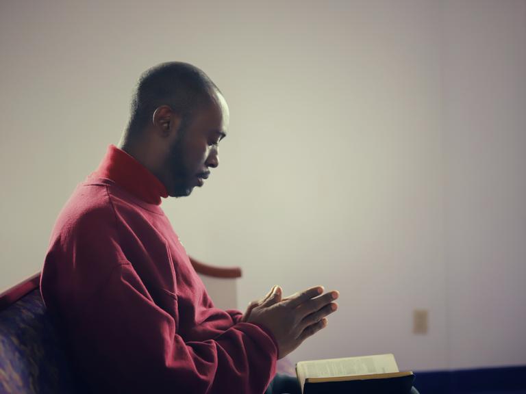 Eine afroamerikanische Person betet in einer Kirche in den USA.