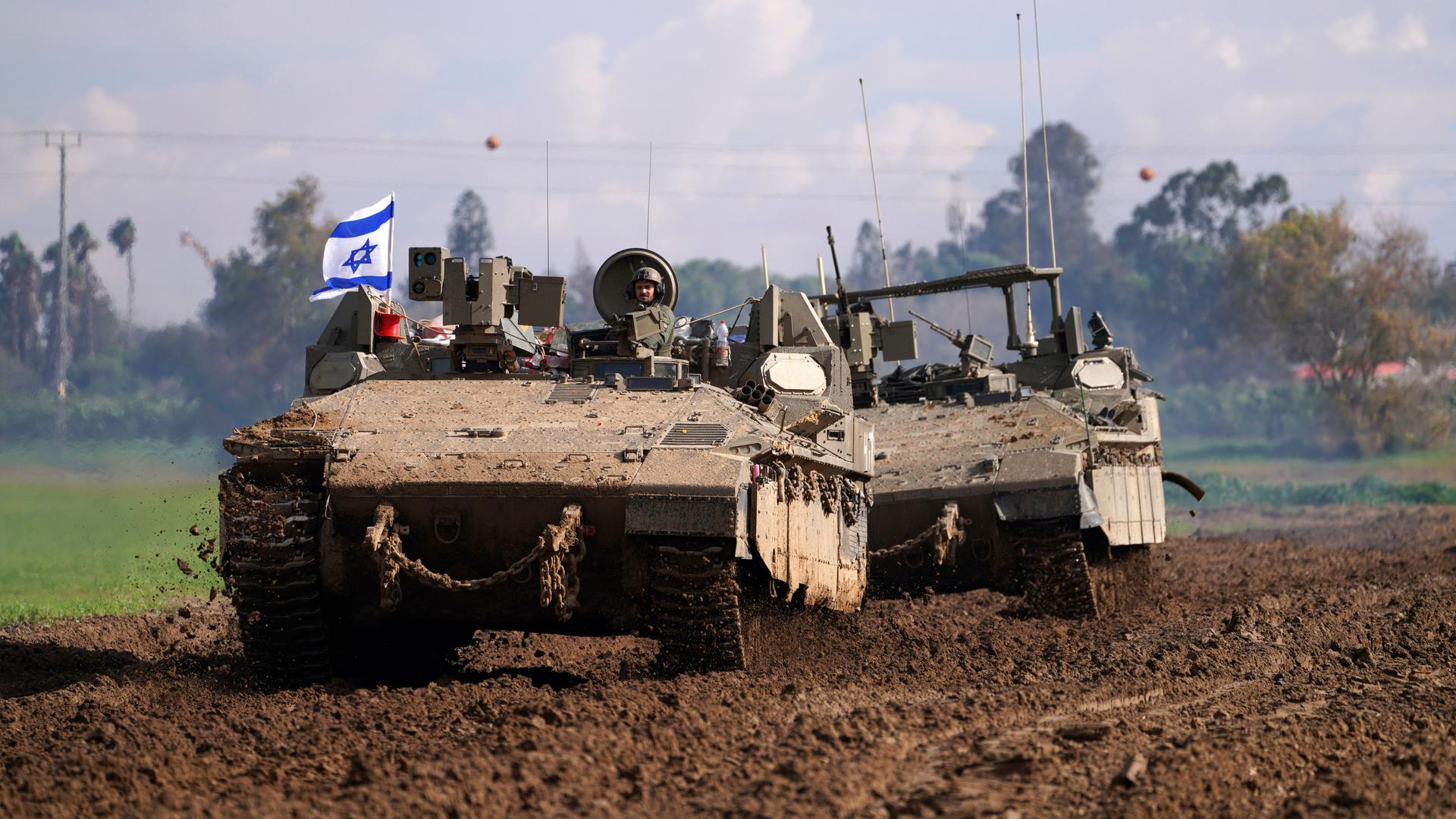 Man sieht einen Panzer und dahinter ein anderes gepanzertes Fahrzeug durch eine schlammige Fläche fahren. Im Hintergrund unscharf eine Baumreihe. Man sieht einen Panzer und dahinter ein anderes gepanzertes Fahrzeug durch eine schlammige Fläche fahren. Im Hintergrund unscharf eine Baumreihe.