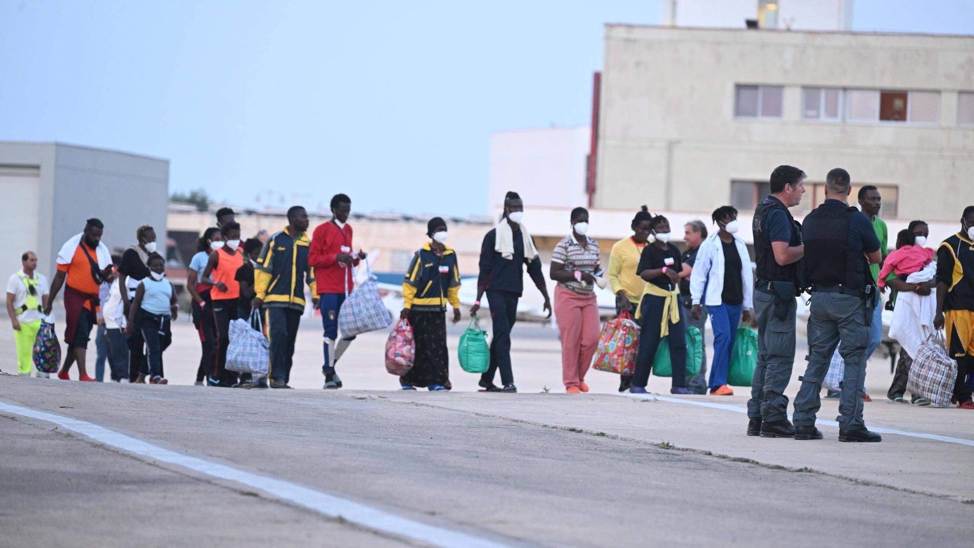 Menschen mit teils großen Gepäckstücken stehen in einer Schlange auf der italienischen Insel Lampedusa.