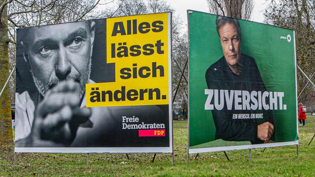 Wahlplakate zur Bundestagswahl 2025 sind zu sehen. Links im Bild ein gelbes Plakat zu Christian Lindner mit der Aufschrift  "Alles lässt sich ändern", rechts im Bild ein Plakat Robert Habeck vor grünen Hintergrund und dem Slogan "Grüne Zuversicht"