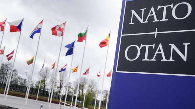 Fahnen der NATO-Mitgliedsstaaten vor dem Brüsseler NATO-Hauptquartier neben einem Schild mit der Aufschrift NATO.