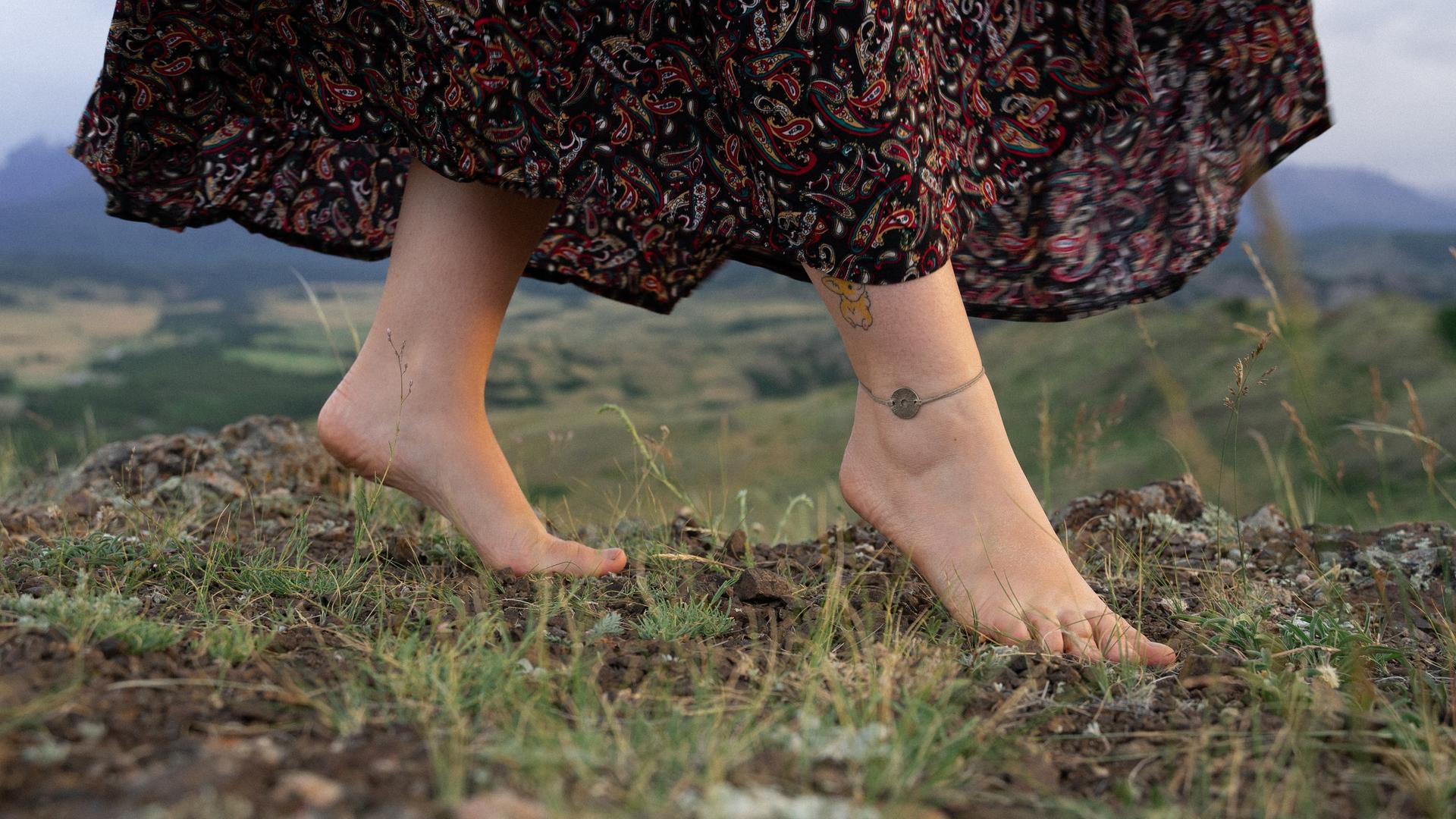 Eine Frau geht barfuß über eine Sommerwiese im Mittelgebirge.