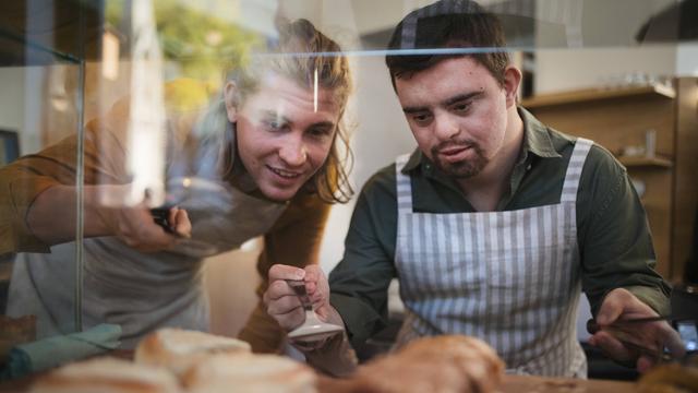 Mann mit Down-Syndrom hilft seinem Kollegen in einem Café. 