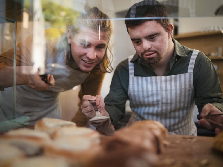 Mann mit Down-Syndrom hilft seinem Kollegen in einem Café. 