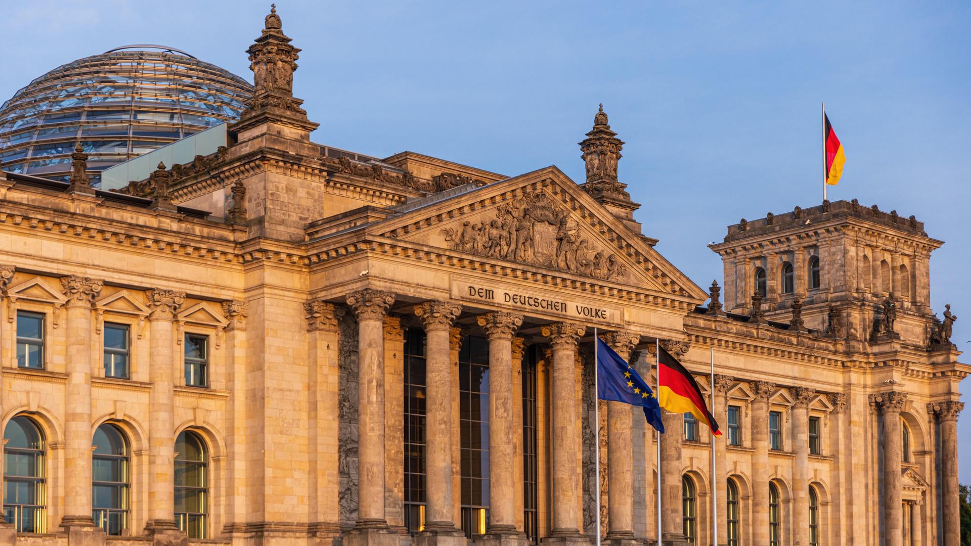 Die deutsche und die europäische Flagge wehen vor dem Reichstagsgebäude in Berlin im Wind.