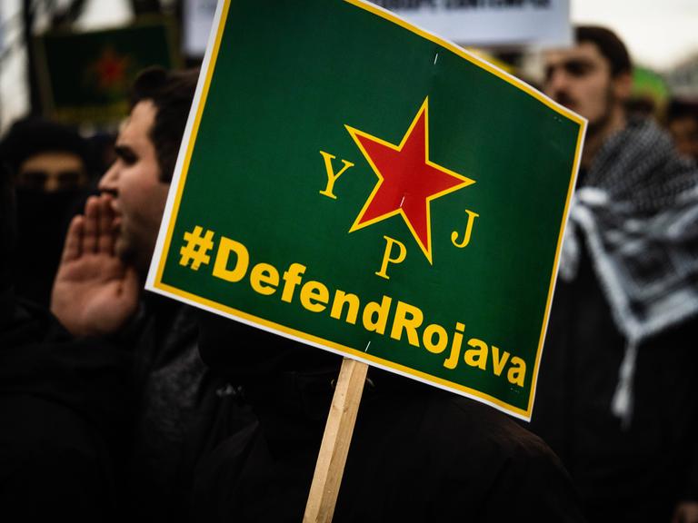 Demonstranten mit einem grünen Schild, auf dem steht "Defend Rokava".