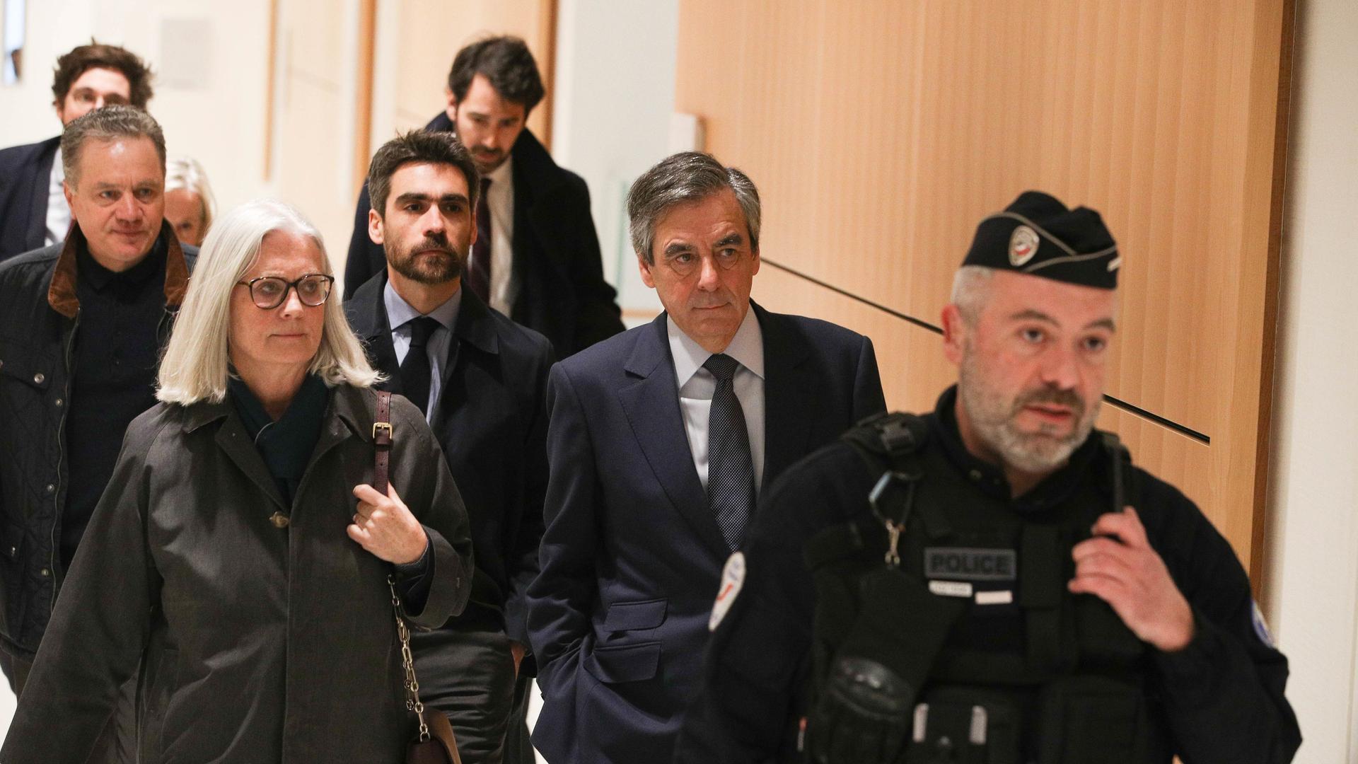 Der ehemalige französische Premierminister Francois Fillon und seine Ehefrau Penelope auf dem Weg zu ihrer Gerichtsverhandlung. Sie werden von einem Polizisten und mehreren weiteren Personen begleitet. Der ehemalige französische Premierminister Francois Fillon und seine Ehefrau Penelope auf dem Weg zu ihrer Gerichtsverhandlung. Sie werden von einem Polizisten und mehreren weiteren Personen begleitet.
