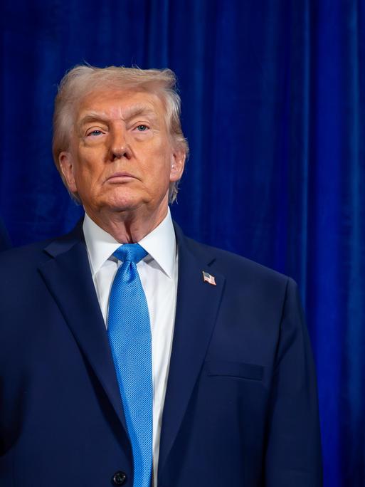 US-Präsident Donald Trump steht vor einem blauen Hintergund und schaut starr nach vorne