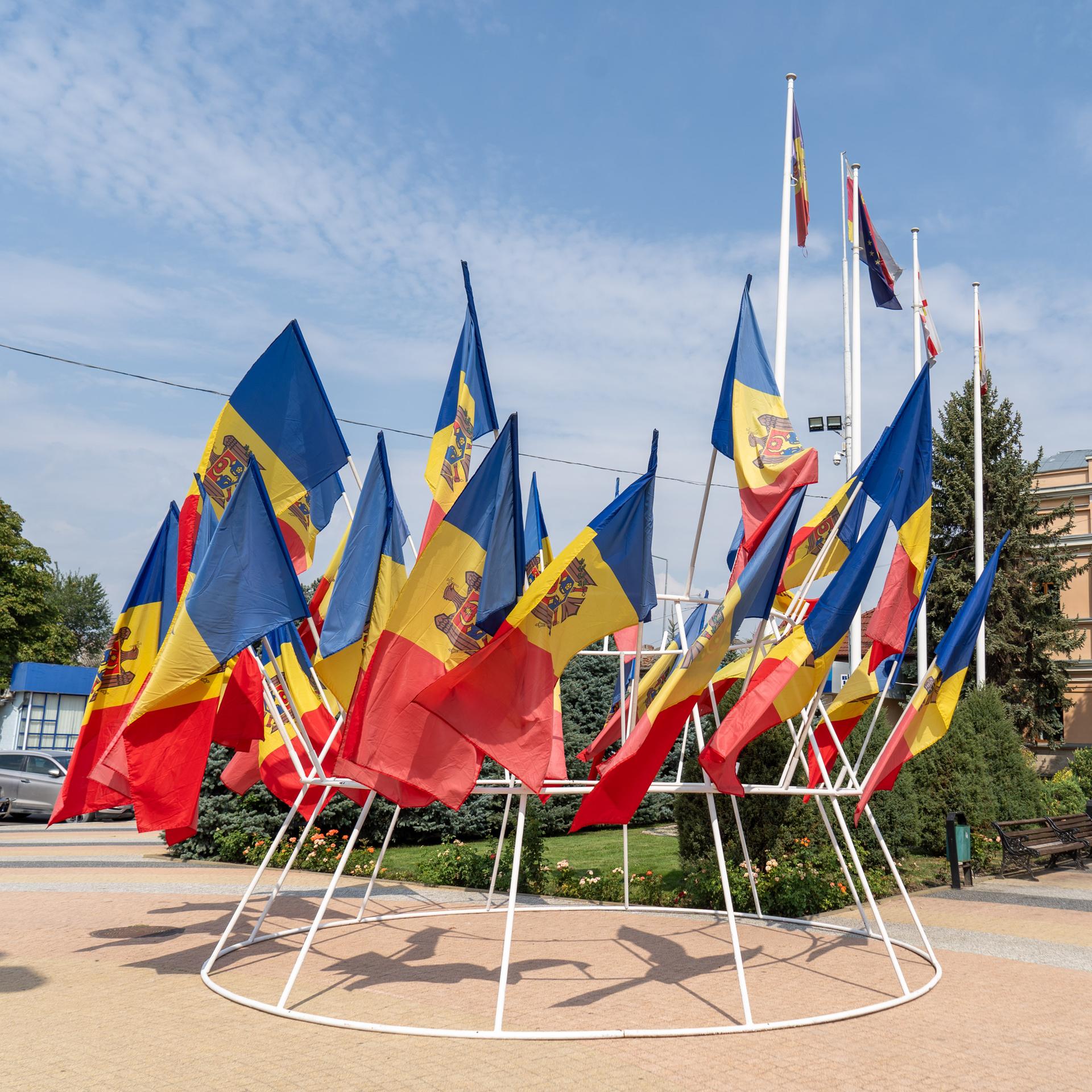Rot-gelb-blaue Nationalflaggen der Republik Moldau wehen auf einem Platz. 