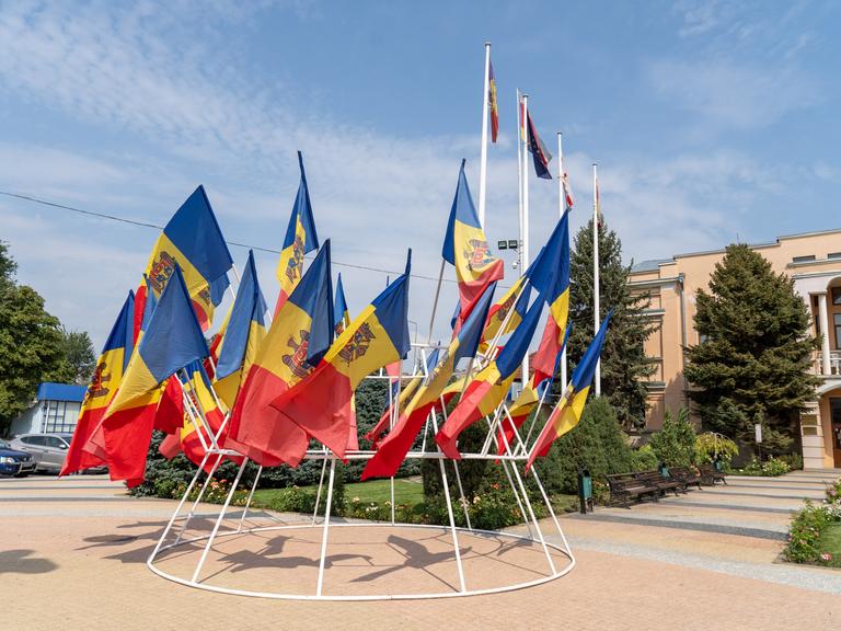 Rot-gelb-blaue Nationalflaggen der Republik Moldau wehen auf einem Platz. 