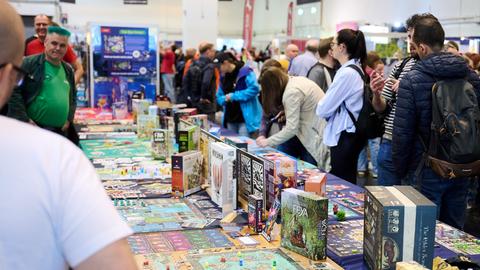 Besucher stehen beim Medien-Rundgang der internationalen Publikumsmesse "Spiel Essen 2025“ in der Messe Essen um einen langen Tisch, auf dem verschiedene Spiele präsentiert werden. 