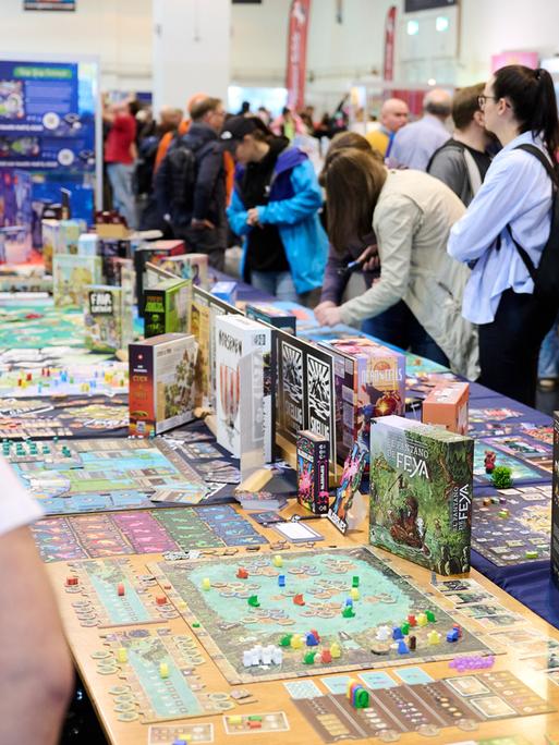 Besucher stehen beim Medien-Rundgang der internationalen Publikumsmesse "Spiel Essen 2025“ in der Messe Essen um einen langen Tisch, auf dem verschiedene Spiele präsentiert werden. 