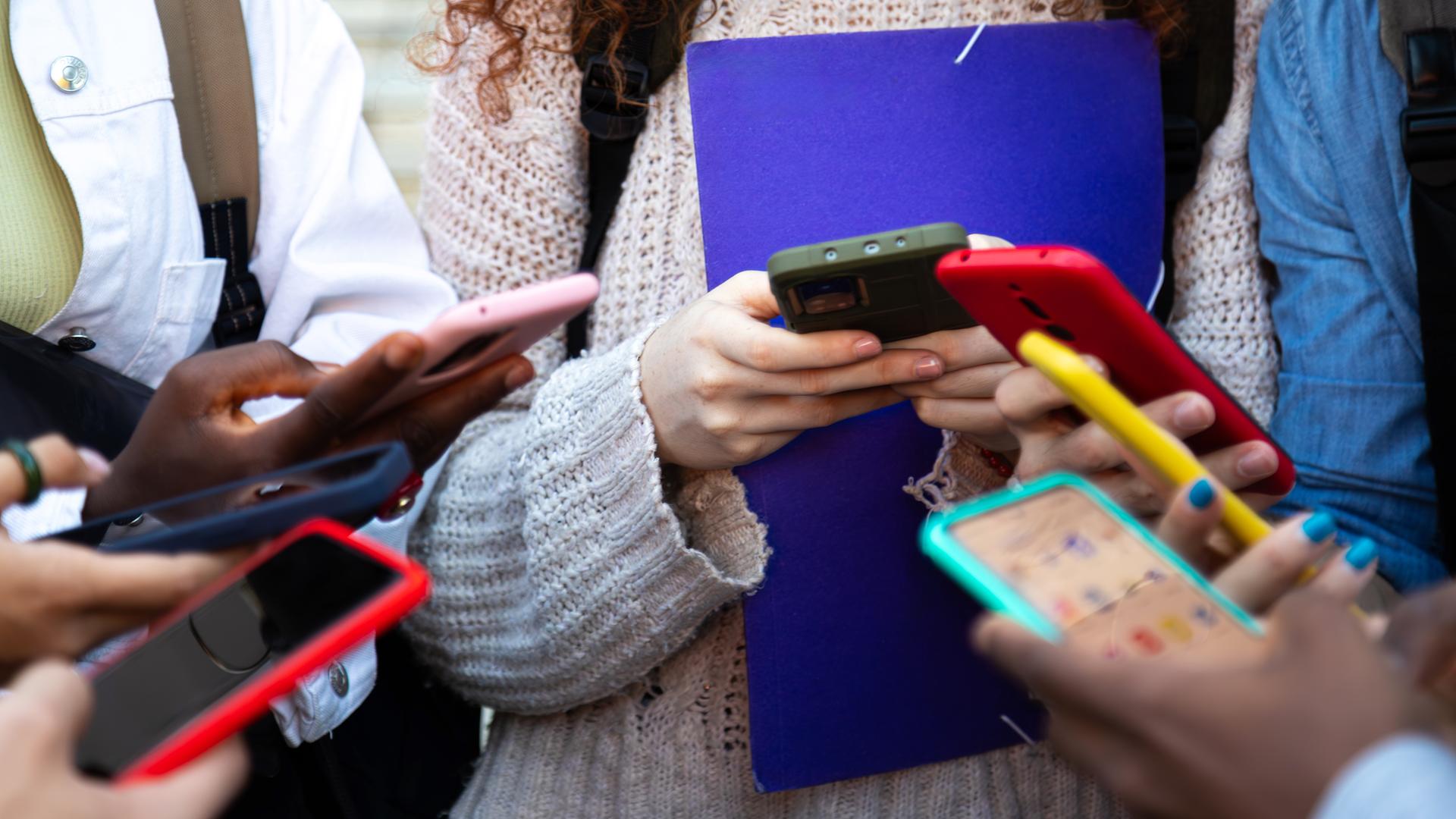 Nahaufnahme von jungen Menschen, die alle ein buntes Smartphone in den Händen halten und bei Social Media Inhalte teilen.