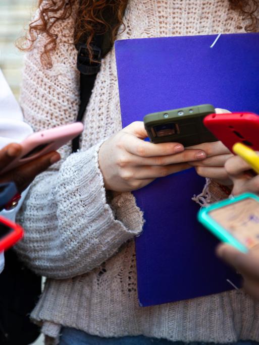 Nahaufnahme von jungen Menschen, die alle ein buntes Smartphone in den Händen halten und bei Social Media Inhalte teilen.