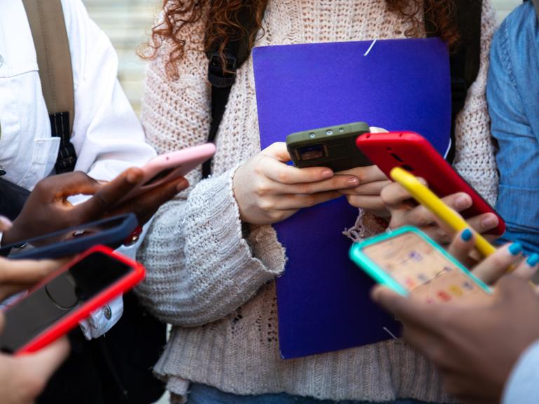 Nahaufnahme von jungen Menschen, die alle ein buntes Smartphone in den Händen halten und bei Social Media Inhalte teilen.